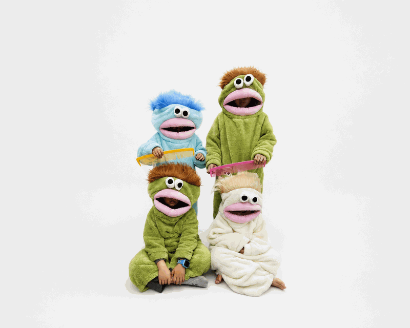 Four children wearing blue, green and white plush monster onesies while posing with oversized colorful combs.