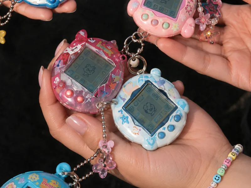 Adults holding a colorful collection of Tamagotchi virtual pets with decorative charms