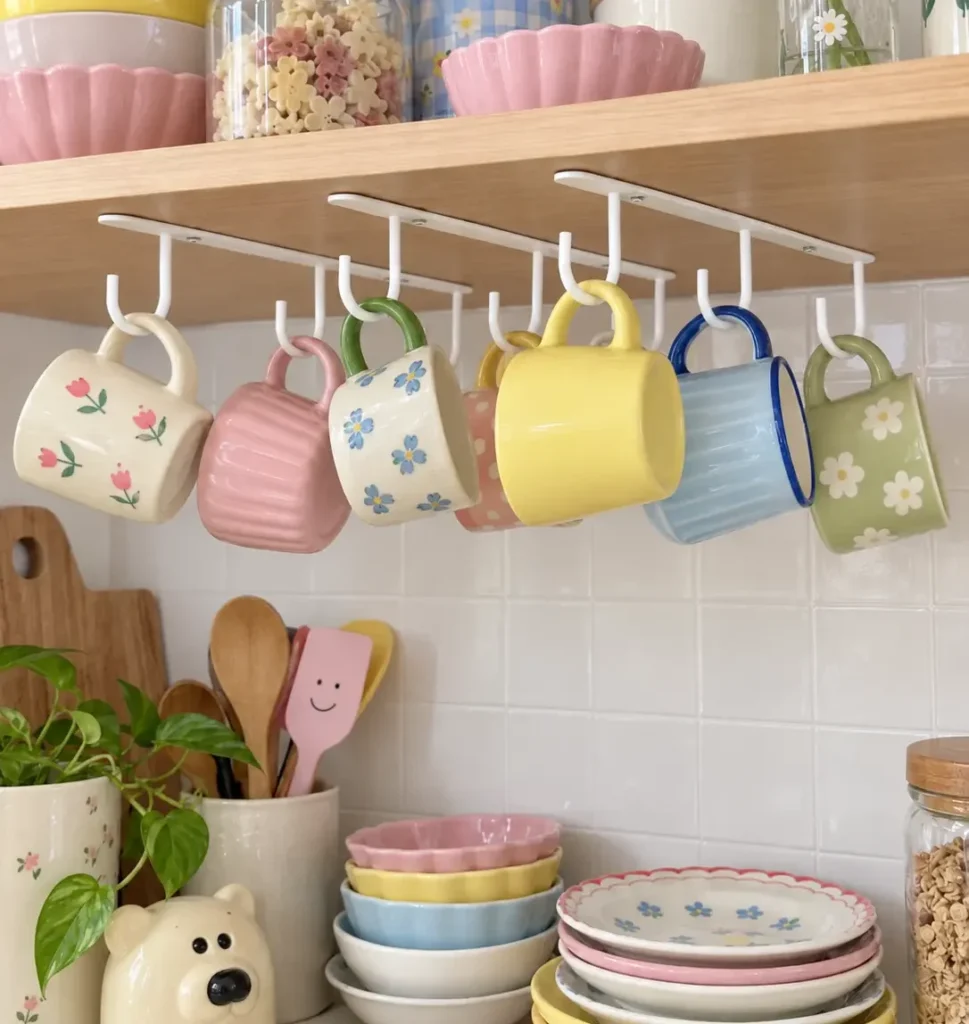Under-cabinet mug hooks holding colorful coffee mugs beneath a wooden kitchen shelf