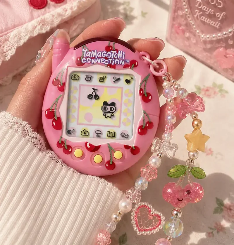 Hand holding a pink cherry Tamagotchi Connection with colorful beaded charms